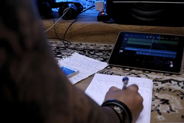 Quelle: arijitsahaofficial/pixelio.de Deutsch: Hand schreibt mit Kugelschreiber auf Notizblock, daneben Smartphone und Tablet mit Musiksoftware auf Teppichboden.